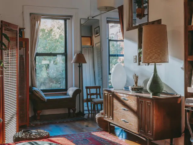 Pokój w stylu vintage z drewnianą komodą, lampą z abażurem, szezlongiem pod oknem i drewnianym parawanem
