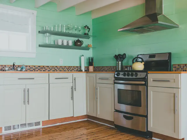 Miętowa ściana z drewnianych desek w kuchni z białymi szafkami, stalowym okapem i otwartymi półkami ze szkłem