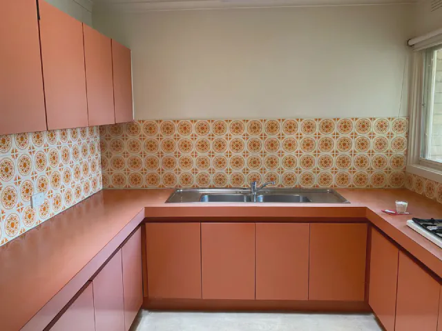 Kuchnia w układzie U z matowymi frontami i blatem w kolorze terakoty oraz płytkami w pomarańczowy wzór retro