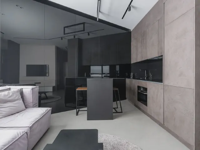 Kuchnia otwarta na salon z wysoką zabudową imitującą beton, czarną wyspą i czarnymi szafkami w tle
