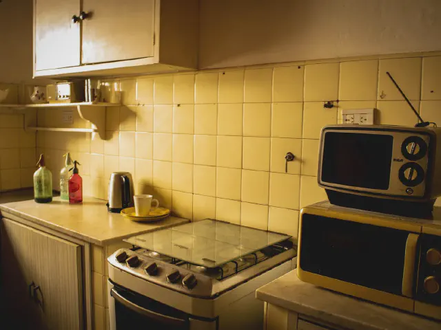 Retro kuchnia z kremowożółtymi płytkami, starą kuchenką gazową, zabytkowym telewizorem i syfonami na półce