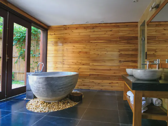 Łazienka w stylu spa z kamienną wanną na podeście z otoczaków, ścianą obłożoną drewnem i drzwiami otwartymi na ogród