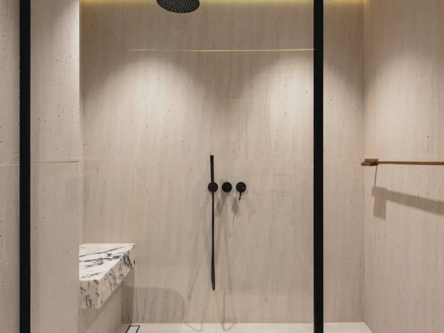 Wnęka prysznicowa walk-in z beżowymi płytkami wielkoformatowymi, szklaną ścianką w czarnym profilu i czarną baterią podtynkową