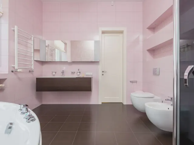 Łazienka z jasnoróżowymi ścianami, ciemnobrązową posadzką, podwieszaną ceramiką, grzejnikiem drabinkowym i wanną
