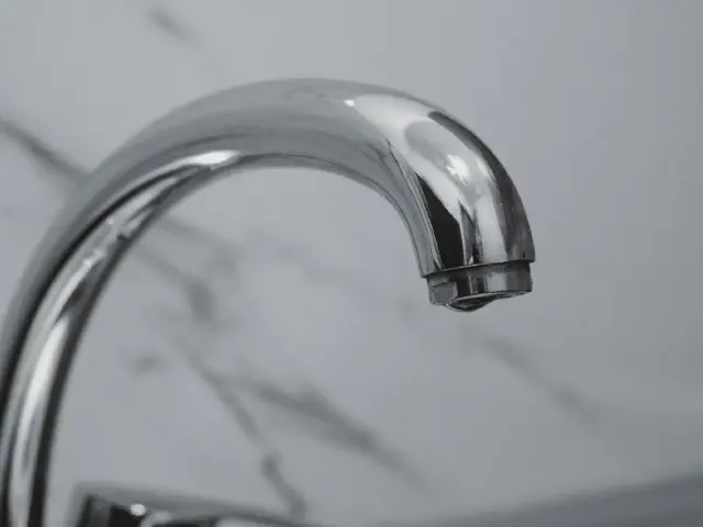 Zbliżenie na chromowaną wylewkę baterii na tle płytek w rysunku białego marmuru