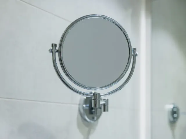 Okrągłe lusterko kosmetyczne na chromowanym ramieniu zamocowane na białej ścianie z płytek