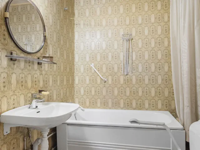 Łazienka w stylu retro z płytkami we wzór w odcieniach żółci i beżu, wanną, białą umywalką i okrągłym lustrem