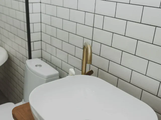 Białe płytki metro na ciemnej fudze na ścianach wokół wanny i toalety, złota bateria i fragment wanny na pierwszym planie