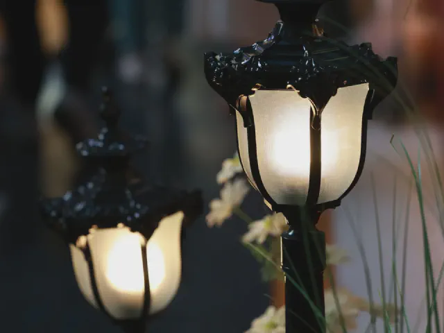 Dwie lampy ogrodowe w kształcie kwiatów tulipana z mlecznymi kloszami świecące wśród traw