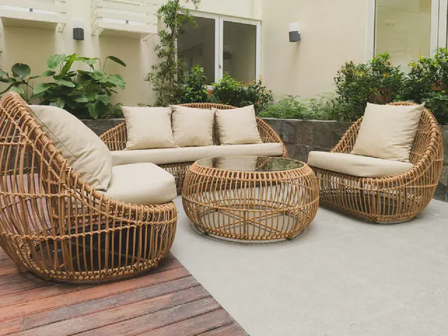 Komplet mebli z naturalnego rattanu: sofa, dwa kuliste fotele i okrągły stolik z jasnymi poduszkami na tarasie przy domu