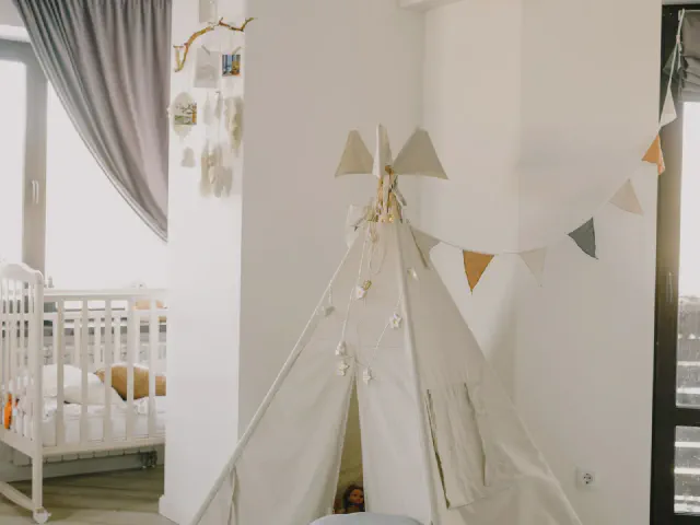 Biały pokój z białym łóżeczkiem, kremowym namiotem tipi i girlandą z trójkątnych chorągiewek