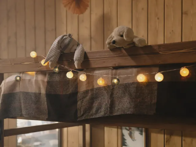 Pluszaki na drewnianym łóżku piętrowym z kraciastym kocem i girlandą świetlną na tle drewnianej boazerii
