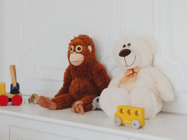 Pluszowy orangutan i biały miś na białej komodzie obok drewnianych zabawek