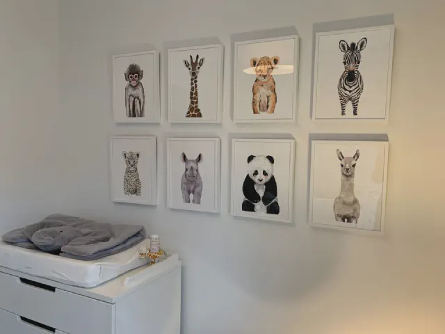 Osiem grafik w białych ramkach z portretami zwierząt – małpa, żyrafa, zebra, lew, panda, lama – nad białą komodą z przewijakiem