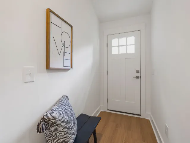 Wąski przedpokój z czarną ławką z poduszką w geometryczny wzór, grafiką z napisem HOME i białymi drzwiami z okienkiem