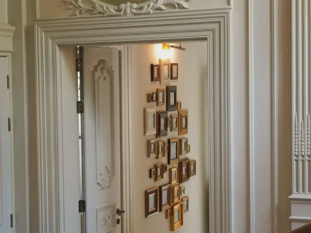 Bogato profilowana opaska wokół otwartych drzwi, na skrzydle kolekcja małych złotych ramek, obok pilaster z ornamentem
