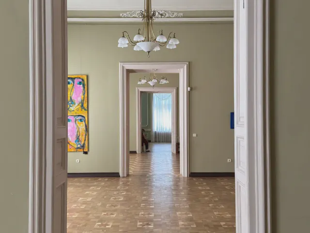 Amfilada pokoi z oliwkowymi ścianami, białymi opaskami drzwi, parkietem w geometryczny wzór i kryształowymi żyrandolami