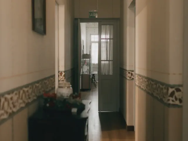 Wąski korytarz ze ścianami w kolorze écru, ozdobnym szlaczkiem tapety na wysokości lamperii i przeszklonymi drzwiami na końcu