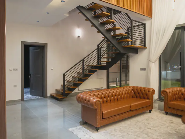 Dwukondygnacyjny salon z czarnymi metalowymi schodami o drewnianych stopniach i brązową sofą chesterfield