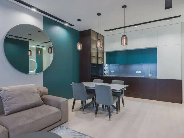 Salon z jadalnią przy morskiej ścianie – szary stół z krzesłami pod rzędem lamp wiszących, na pierwszym planie szara sofa