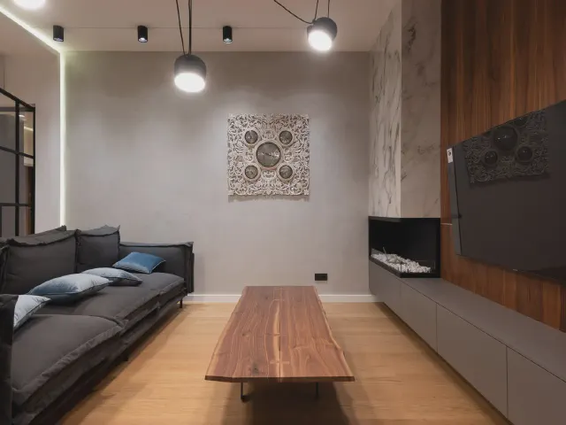 Nowoczesny salon z biokominkiem wbudowanym w długą szafkę RTV pod okładziną imitującą marmur, grafitowa sofa i stolik z litego drewna