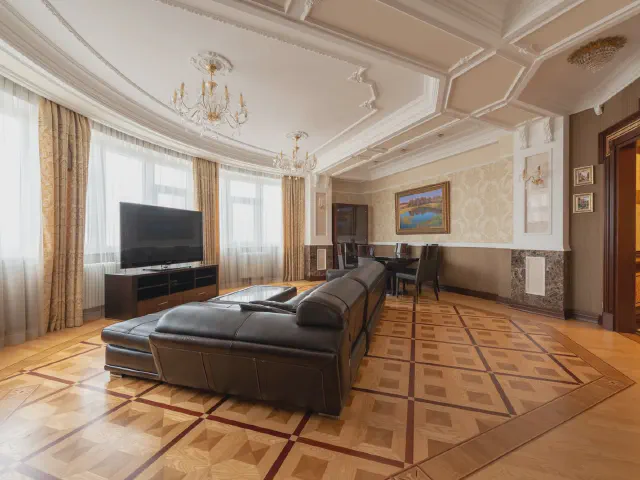 Klasyczny salon ze sztukaterią na suficie i kremowymi ścianami, czarna skórzana sofa na parkiecie ułożonym w geometryczny wzór