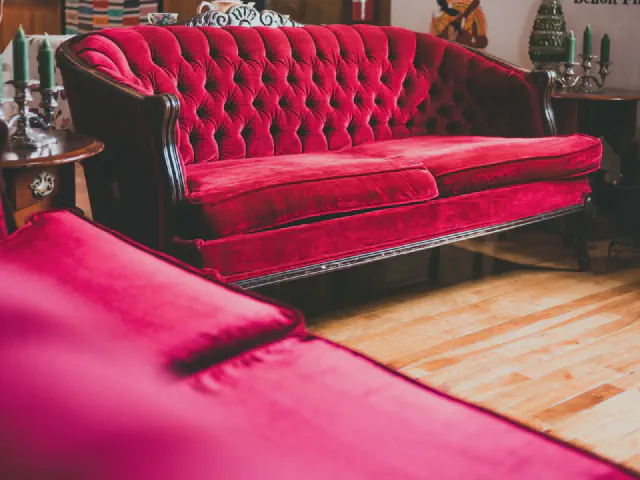 Malinowa pikowana sofa z welurowym obiciem i rzeźbioną ciemną ramą na jasnej drewnianej podłodze