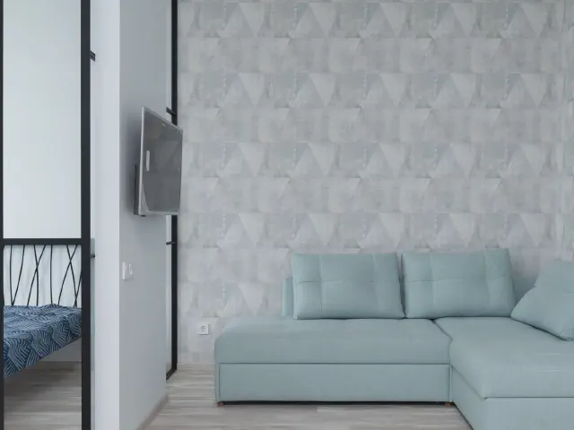 Miętowa sofa narożna na tle ściany z jasnoszarą tapetą w geometryczny wzór i telewizora na ścianie