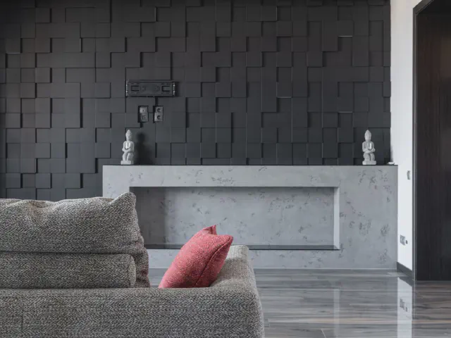 Szara sofa z czerwoną poduszką przed czarną ścianą z trójwymiarowych kostek i betonową konsolą