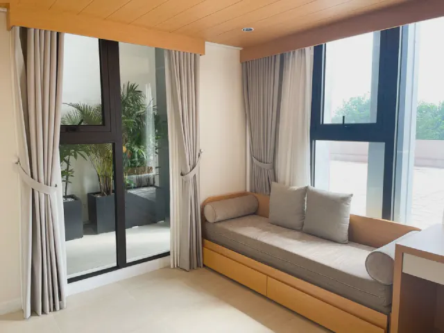 Jasny salon z przeszklonymi drzwiami na taras i dużym oknem, szarobeżowe zasłony do podłogi upięte opaskami, pod oknem niska sofa z szarymi poduszkami