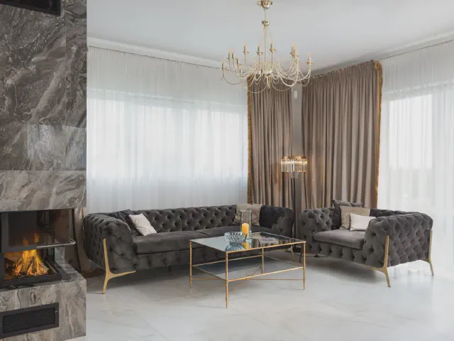 Salon glamour z pikowanymi sofami chesterfield, kryształowym żyrandolem i kominkiem w marmurowej obudowie