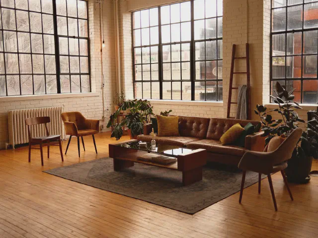 Loft z wysokimi oknami w stalowych ramach, brązową skórzaną sofą i drewnianą podłogą