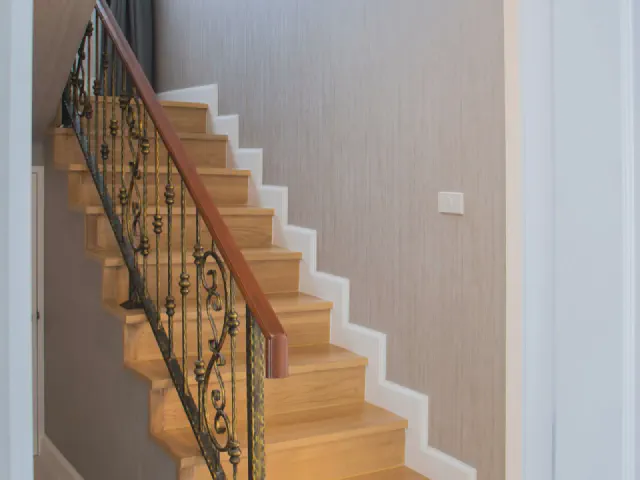 Drewniane schody wzdłuż ściany z balustradą z kutych tralek w ornamentowy wzór i drewnianą poręczą