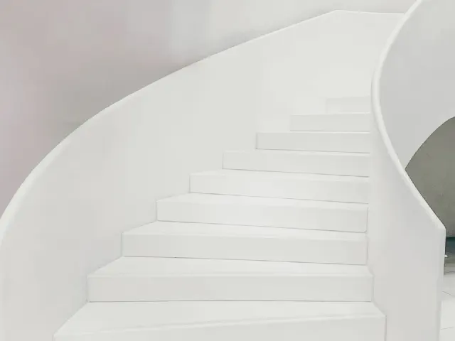 Białe, łukowe schody z pełną, otynkowaną balustradą poprowadzoną płynnie wzdłuż biegu