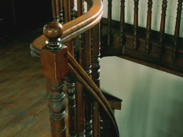 Zbliżenie na ciemnobrązową, toczoną drewnianą balustradę i słupek z gałką na starych schodach