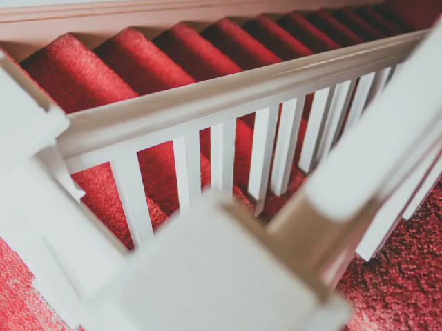 Widok z góry na schody z czerwoną wykładziną i białą balustradą z płaskimi tralkami