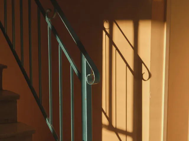 Schody z miętową, metalową balustradą przy ciepłej, pomarańczowej ścianie oświetlonej słońcem