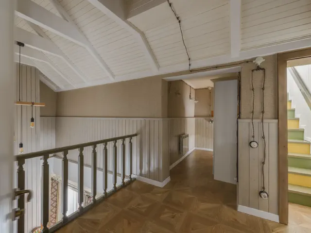 Antresola z drewnianą balustradą, w głębi schody z podstopnicami pomalowanymi na różne kolory