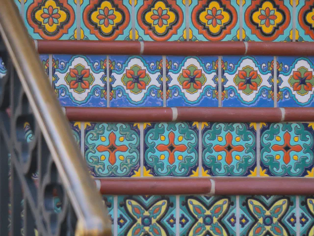 Podstopnice wyłożone kolorowymi płytkami ceramicznymi w orientalne wzory, drewniane krawędzie stopni i kuta balustrada