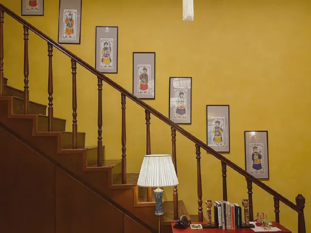 Drewniane schody z toczonymi tralkami przy musztardowej ścianie z galerią oprawionych grafik