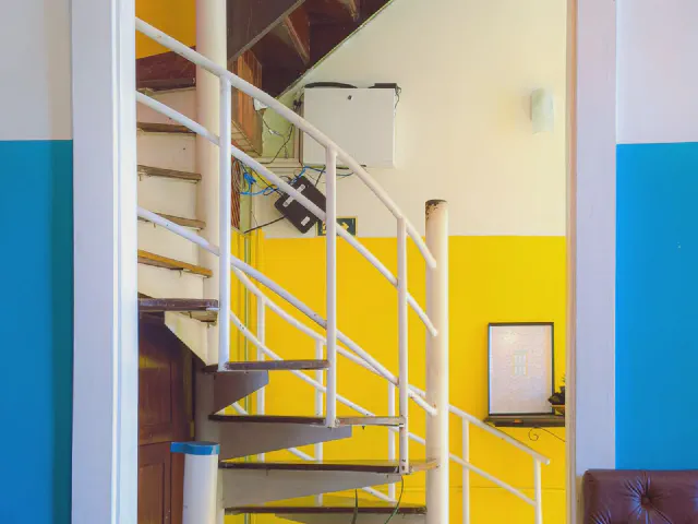 Białe schody kręcone z metalową balustradą na tle ścian pomalowanych w intensywnie żółte i niebieskie pola