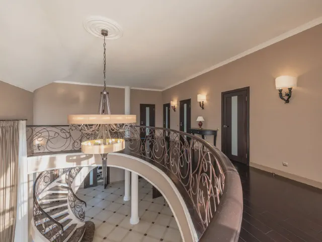 Hol na piętrze z zaokrągloną antresolą, kutą balustradą w ornamenty, lampą wiszącą nad klatką schodową i marmurową posadzką w dole