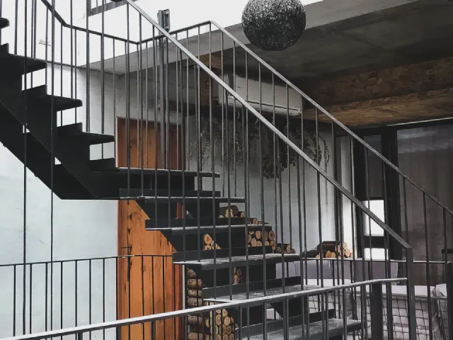 Czarne stalowe schody ze stopniami z blachy i balustradą z pionowych prętów przy ścianie z drewnianych desek