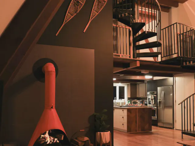 Wnętrze w stylu mid-century z czerwonym wiszącym kominkiem, stalowymi schodami spiralnymi na antresolę i kuchnią w głębi