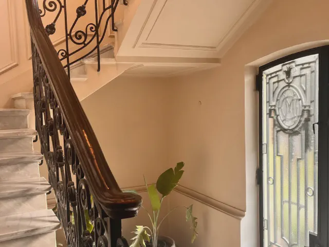 Schody z kutą, ozdobną balustradą i drewnianym pochwytem, skręcające przy drzwiach wejściowych z ozdobnym szkłem