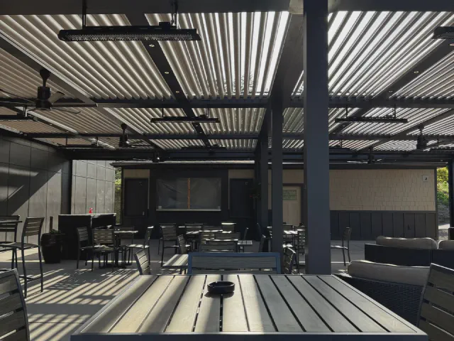Pergola z aluminiowymi lamelami nad dużym tarasem z metalowymi meblami, stołem i strefą wypoczynku