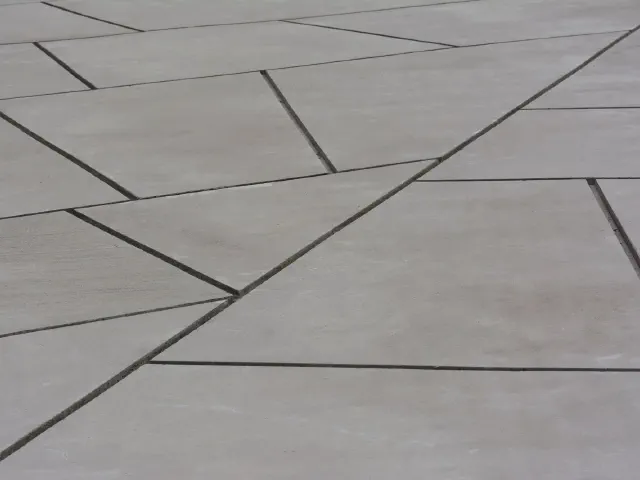 Zbliżenie jasnoszarych wielkoformatowych płyt betonowych ułożonych w nieregularny, geometryczny wzór z wąskimi fugami