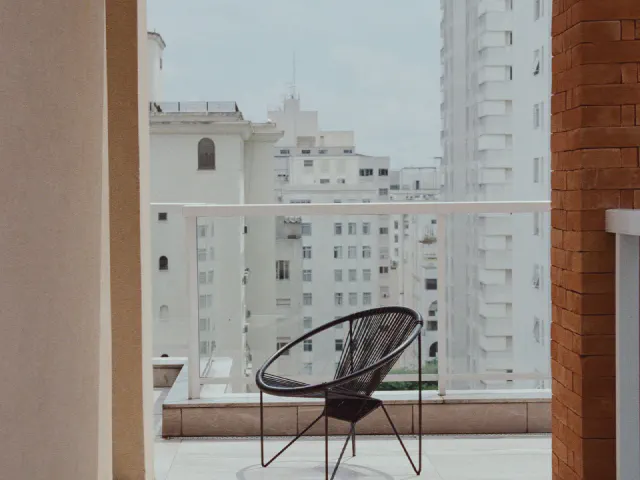 Czarne krzesło z plecionym siedziskiem na nowoczesnym balkonie z przeszkloną balustradą, w tle wieżowce